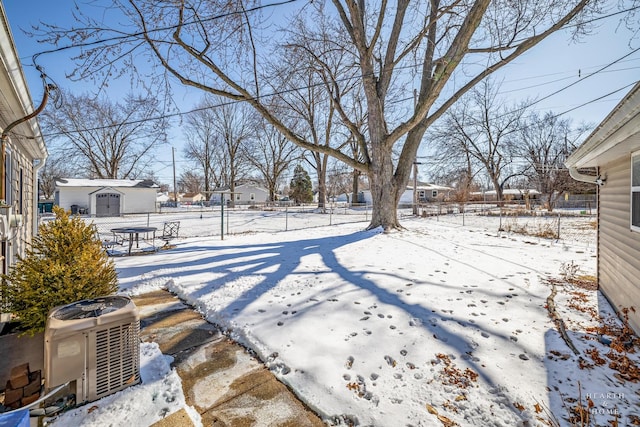 yard layered in snow with central AC, a storage unit, an outdoor structure, and fence