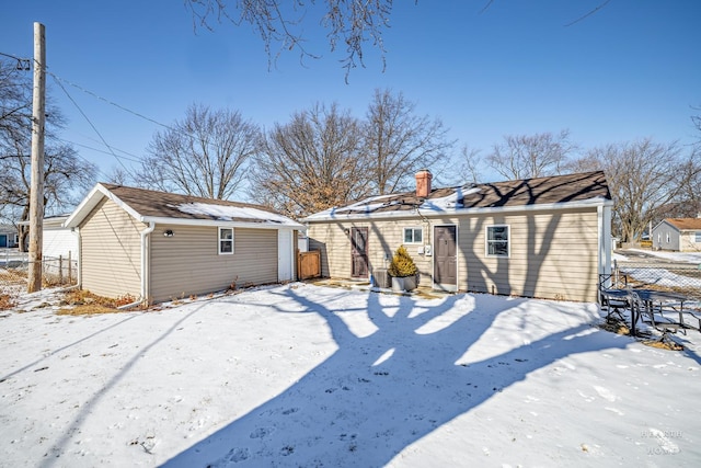 snow covered rear of property featuring a detached garage, a chimney, an outdoor structure, and fence