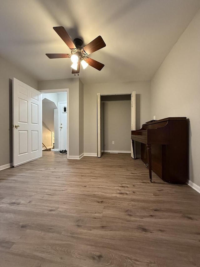 interior space featuring ceiling fan, a closet, baseboards, and wood finished floors