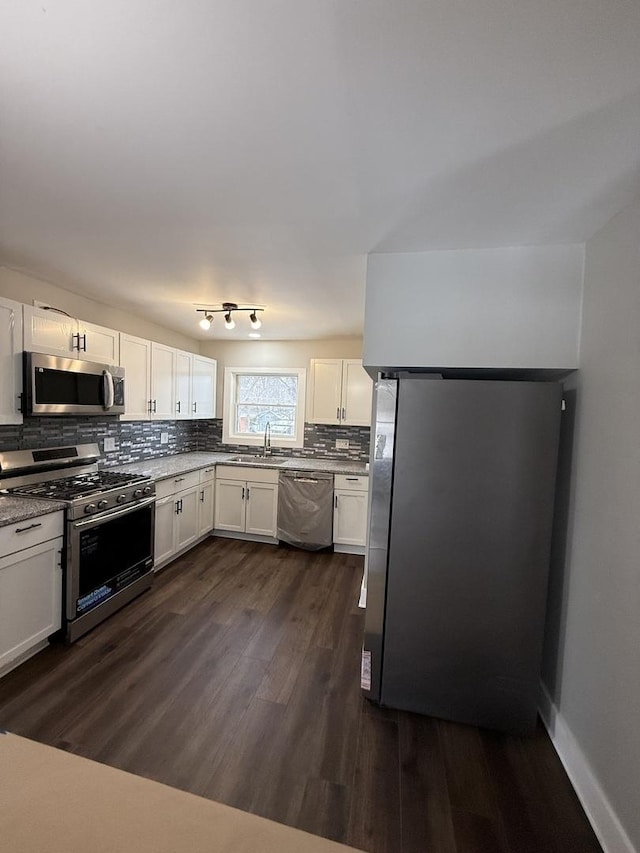 kitchen with dark wood finished floors, stainless steel appliances, decorative backsplash, white cabinetry, and a sink