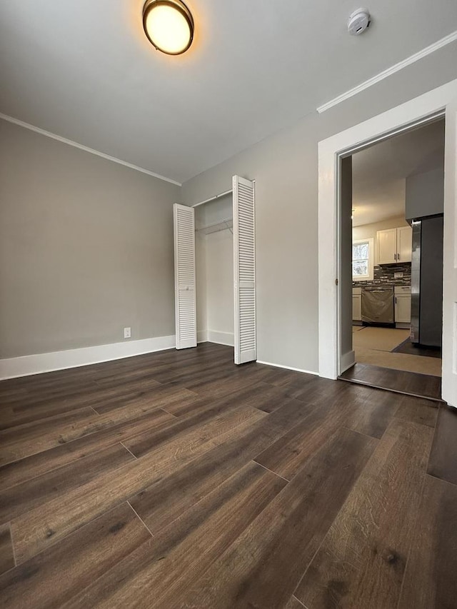 unfurnished bedroom with dark wood-style floors, a closet, freestanding refrigerator, and crown molding