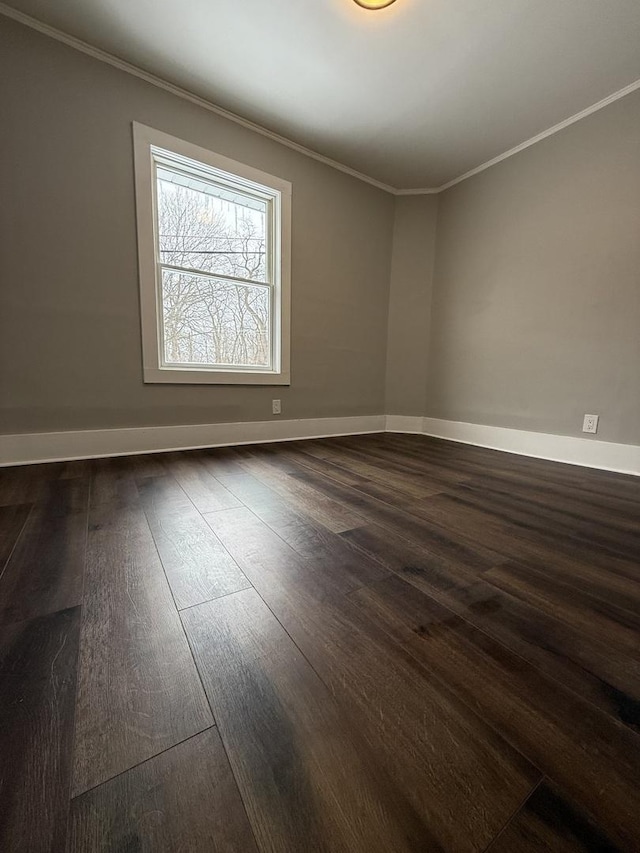 empty room with dark wood-style floors, crown molding, and baseboards