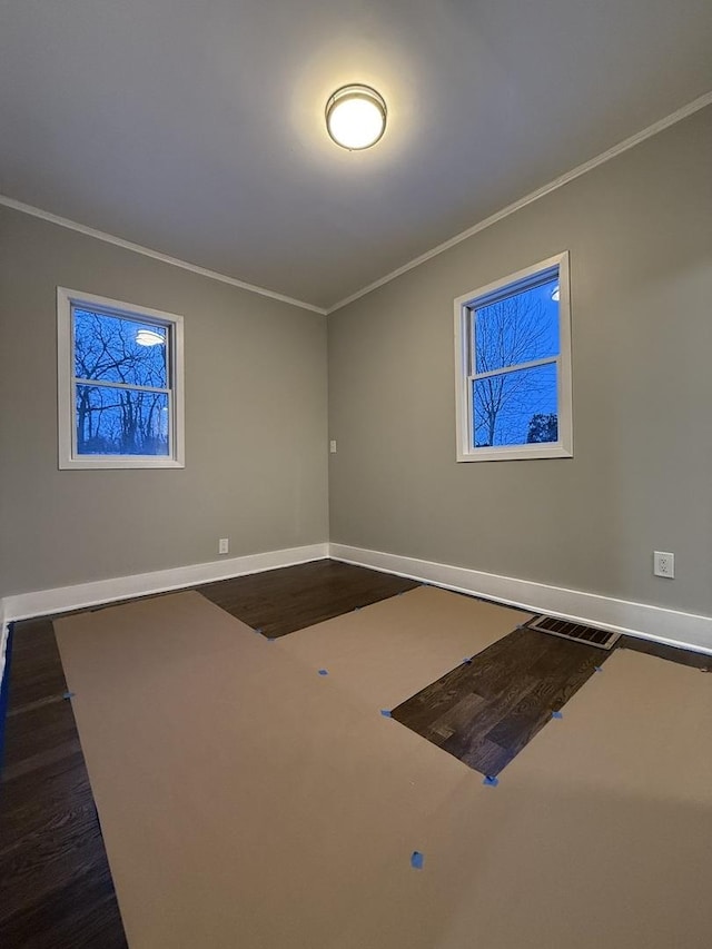 spare room with dark wood finished floors, visible vents, crown molding, and baseboards