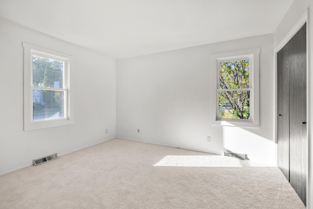 spare room featuring light carpet, plenty of natural light, and visible vents