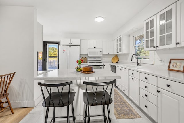 kitchen featuring white appliances, a breakfast bar area, glass insert cabinets, light countertops, and a sink