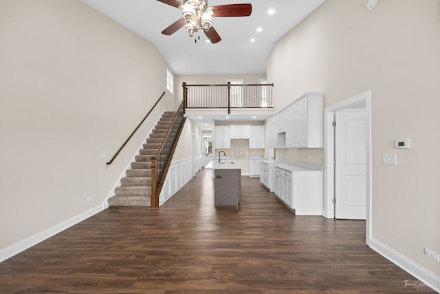 unfurnished living room with dark wood finished floors, a sink, stairway, and baseboards