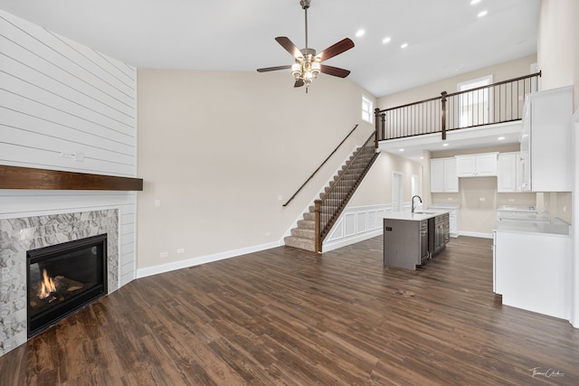 unfurnished living room with a high ceiling, a sink, stairs, dark wood-style floors, and a glass covered fireplace