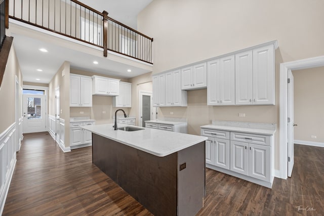 kitchen with white cabinets, an island with sink, dark wood-style floors, a towering ceiling, and a sink