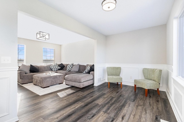 living area with dark wood-type flooring, wainscoting, visible vents, and a decorative wall