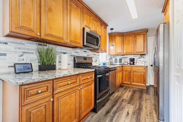 kitchen featuring pendant lighting, stainless steel appliances, backsplash, brown cabinetry, and light stone countertops