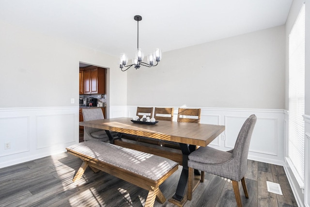 dining area with a chandelier, wainscoting, dark wood finished floors, and a decorative wall