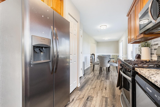 kitchen featuring tasteful backsplash, a wainscoted wall, brown cabinets, stainless steel appliances, and light wood-style floors