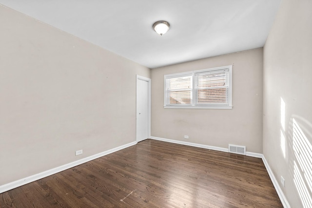 empty room featuring dark wood-style floors, baseboards, and visible vents