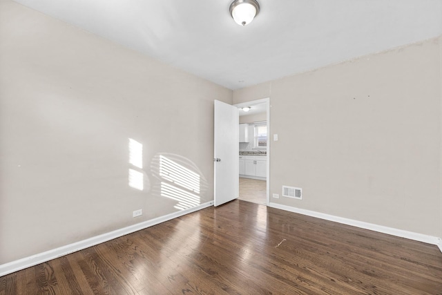 spare room with baseboards, visible vents, and dark wood finished floors