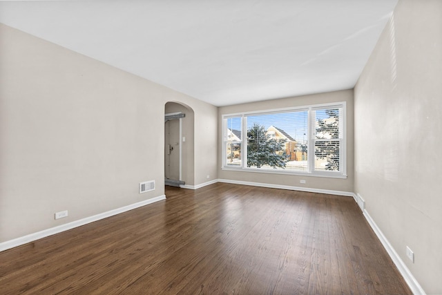 empty room featuring baseboards, visible vents, arched walkways, and dark wood-type flooring