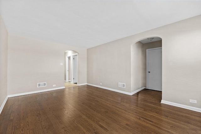 empty room with arched walkways, dark wood-type flooring, visible vents, and baseboards