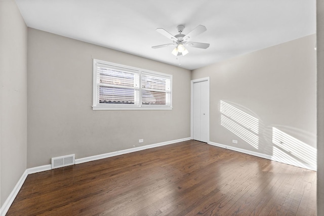 empty room featuring dark wood-style floors, ceiling fan, visible vents, and baseboards