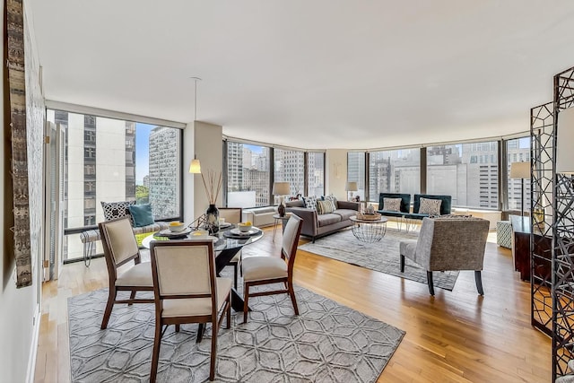 dining space featuring light wood-style floors, a wall of windows, and a city view