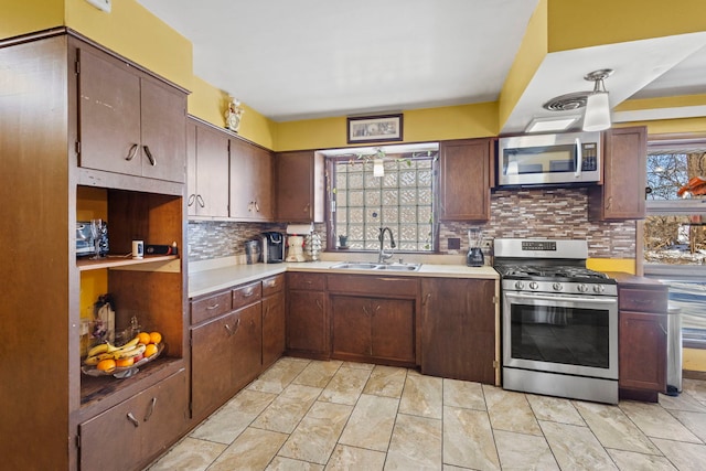 kitchen with pendant lighting, light countertops, backsplash, appliances with stainless steel finishes, and a sink