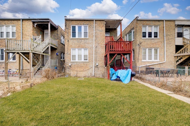 rear view of house featuring a yard, brick siding, stairway, and fence