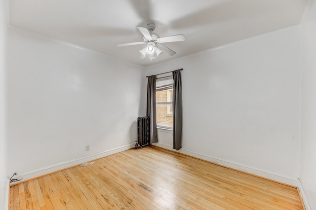 spare room with baseboards, ceiling fan, radiator heating unit, and wood finished floors