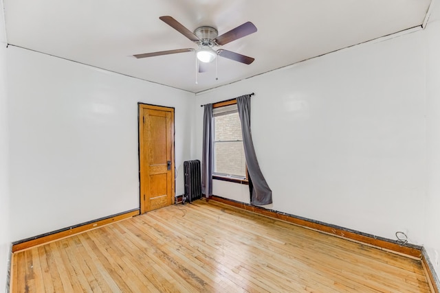 unfurnished room with wood finished floors, a ceiling fan, and radiator