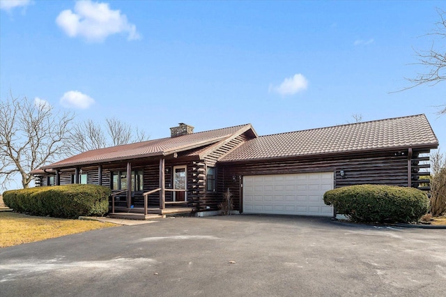 cabin featuring aphalt driveway, a garage, covered porch, log exterior, and a chimney