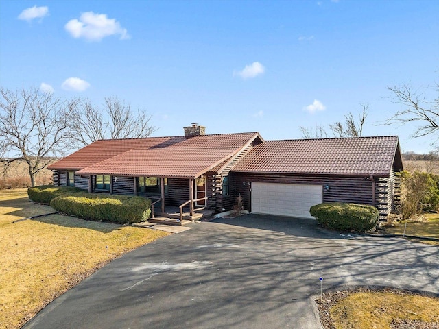 view of front of home with an attached garage, driveway, a chimney, and a tiled roof