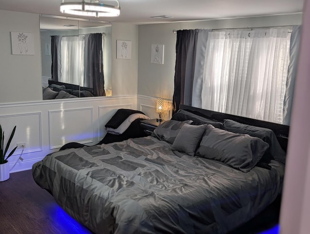 bedroom featuring a wainscoted wall, wood finished floors, visible vents, and a decorative wall