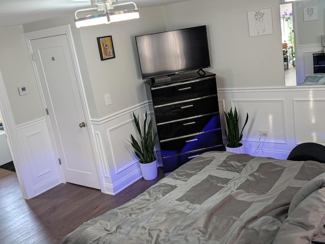 bedroom with dark wood-style floors, a wainscoted wall, and a decorative wall