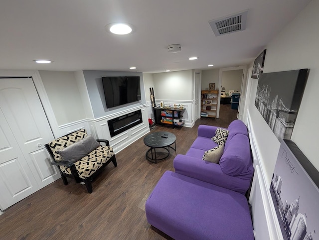 living area featuring recessed lighting, visible vents, dark wood-type flooring, a glass covered fireplace, and wainscoting