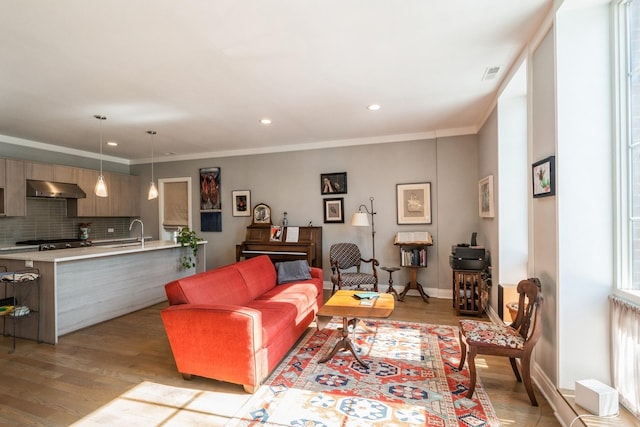 living room with baseboards, visible vents, ornamental molding, light wood-style floors, and recessed lighting