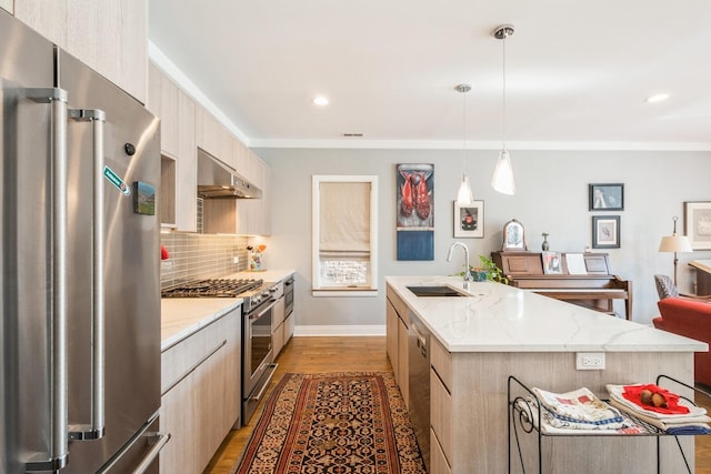 kitchen with pendant lighting, high end appliances, a sink, an island with sink, and under cabinet range hood