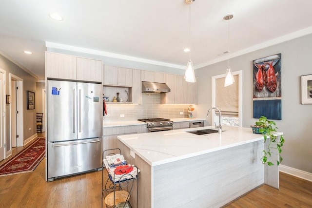 kitchen featuring high end appliances, light stone counters, hanging light fixtures, under cabinet range hood, and a sink