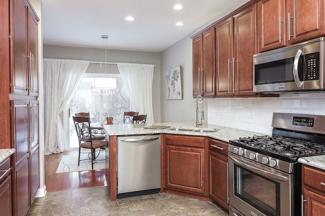 kitchen featuring stainless steel appliances, a peninsula, a sink, tasteful backsplash, and decorative light fixtures