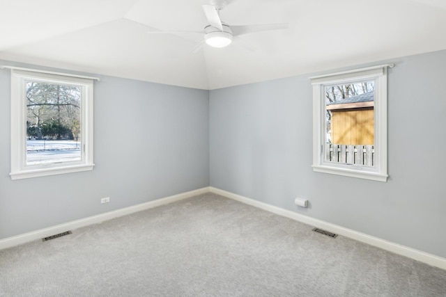 empty room featuring lofted ceiling, a wealth of natural light, visible vents, and carpet flooring