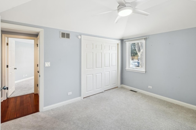 unfurnished bedroom with lofted ceiling, a closet, visible vents, and light colored carpet