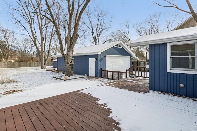 snow covered deck featuring an outbuilding, a detached garage, and fence