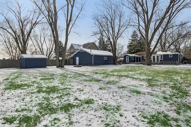 yard covered in snow featuring a storage unit, an outdoor structure, and fence