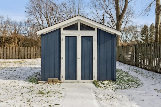 snow covered structure with a fenced backyard, a storage unit, and an outdoor structure