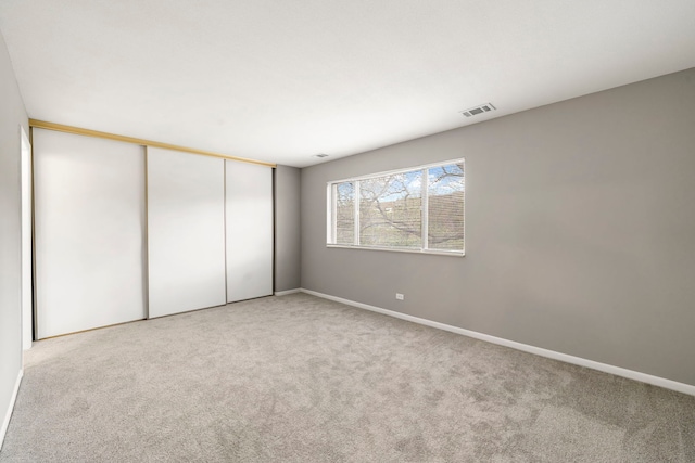 unfurnished bedroom with a closet, light colored carpet, visible vents, and baseboards