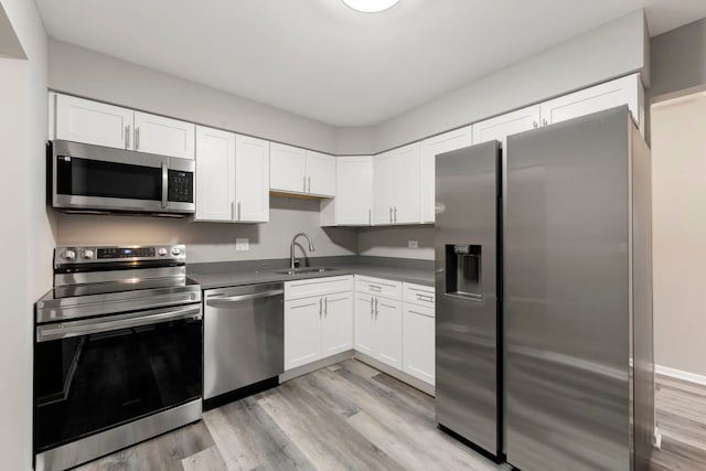 kitchen featuring dark countertops, stainless steel appliances, light wood-style floors, white cabinetry, and a sink