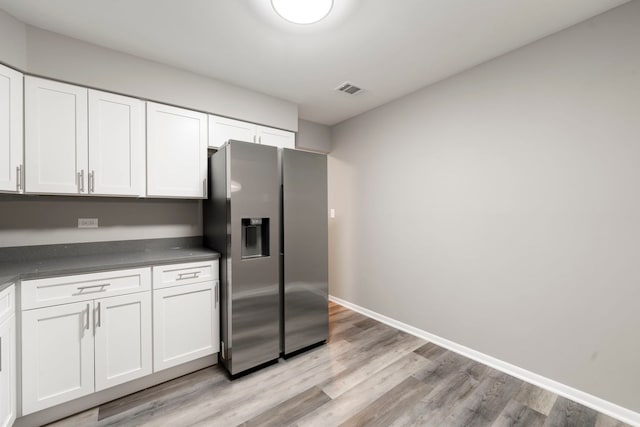 kitchen with light wood-style floors, baseboards, white cabinets, stainless steel refrigerator with ice dispenser, and dark countertops