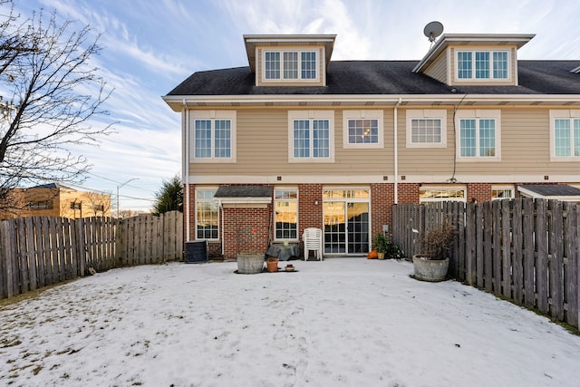 snow covered rear of property featuring a fenced backyard, cooling unit, and brick siding