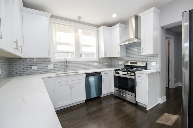 kitchen with wall chimney exhaust hood, light stone countertops, stainless steel appliances, white cabinetry, and a sink