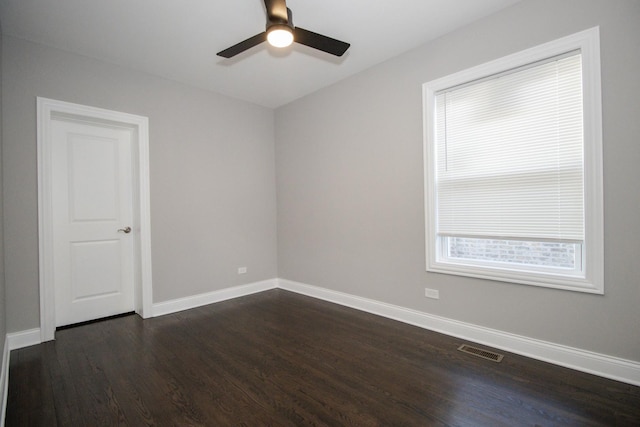 empty room with dark wood-type flooring, visible vents, ceiling fan, and baseboards