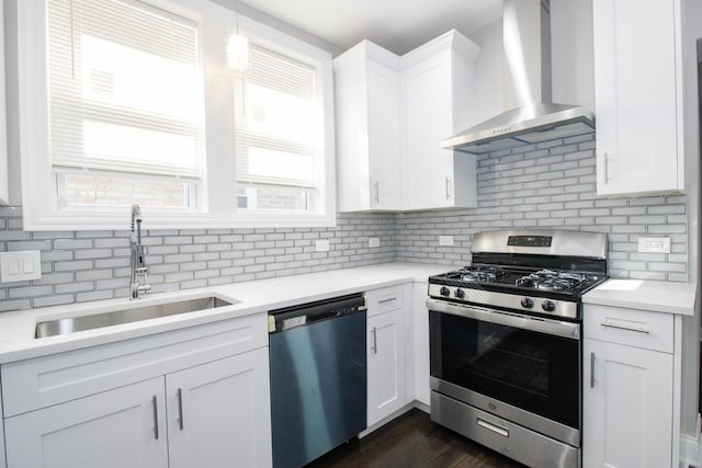 kitchen featuring stainless steel appliances, a sink, white cabinets, light countertops, and wall chimney range hood