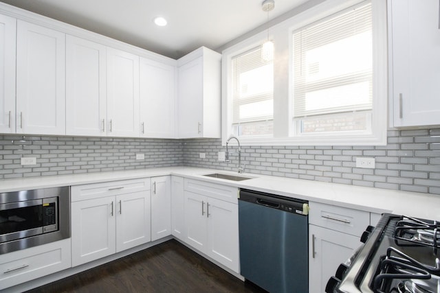 kitchen featuring dark wood-style floors, stainless steel appliances, hanging light fixtures, white cabinetry, and a sink