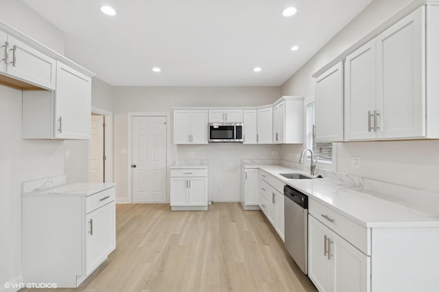 kitchen with appliances with stainless steel finishes, light wood-type flooring, a sink, recessed lighting, and white cabinets