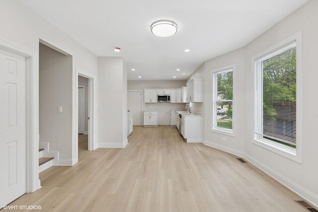 kitchen featuring stainless steel microwave, light wood-style flooring, white cabinets, and baseboards